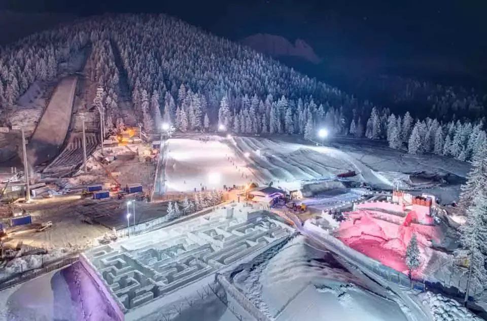 Snowlandia nocą z lotu ptaka: oświetlona górka saneczkowa, śnieżny labirynt i podświetlony lodowy zamek pod Wielką Krokwią
